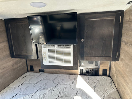 Inside an rv rental: Cozy sleeping area with a bed, mounted TV, Frigidaire AC unit, dark wood cabinets, and outlets.