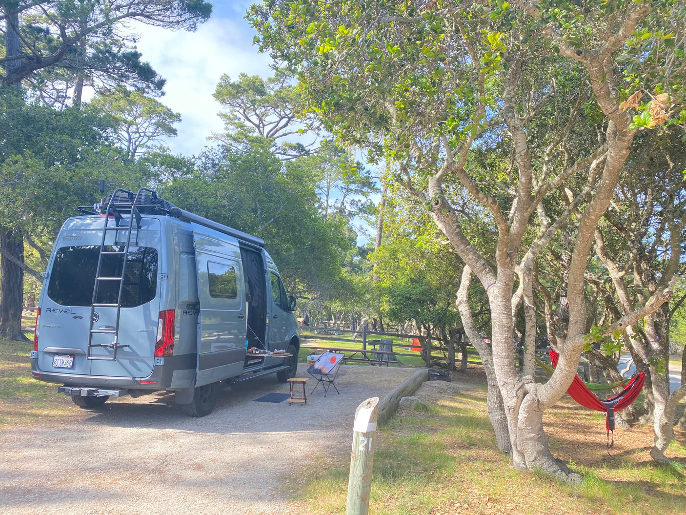 Spacious Winnebago Revel RV rental parked at a tranquil campsite amidst trees with hammocks. Perfect for outdoor adventure.