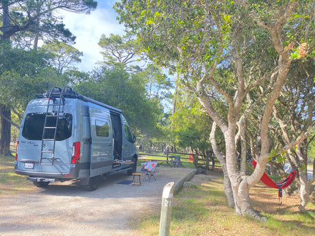 Spacious Winnebago Revel RV rental parked at a tranquil campsite amidst trees with hammocks. Perfect for outdoor adventure.
