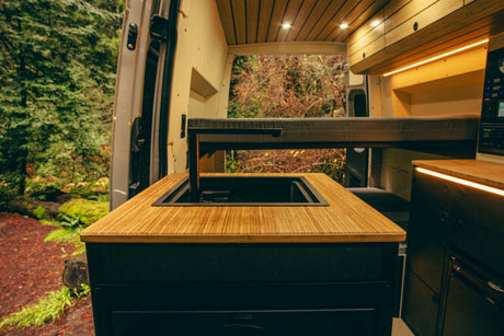 Cozy rv rental interior with custom wood finishes, a kitchen sink, and a bed, opening to a serene forest view.