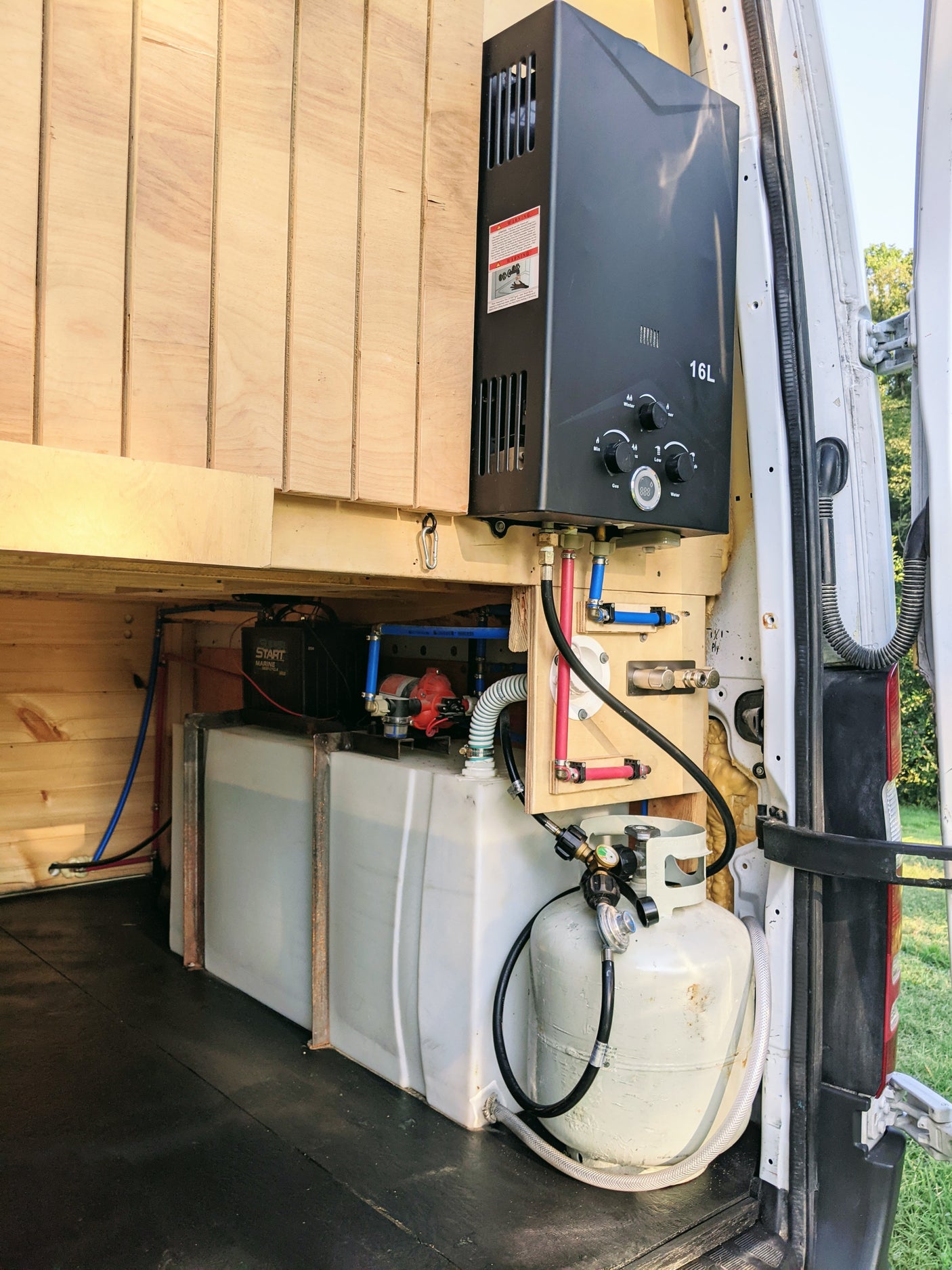 Inside an RV rental: a compact hot water system with propane tank, water tanks, pump, and heater for van life.