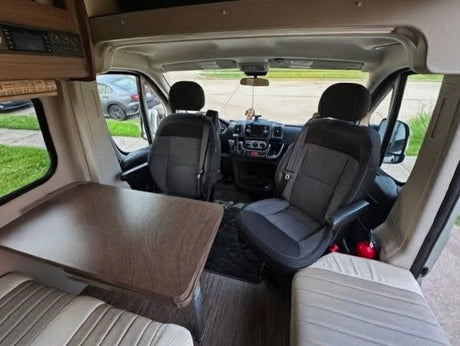RV rental interior: Looking forward from the dining area into the front cab, with swivel seats, table, and bench seating.
