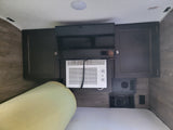 Inside an RV rental bedroom: mounted TV, window AC unit, wood-look cabinets, and a comfortable bed.
