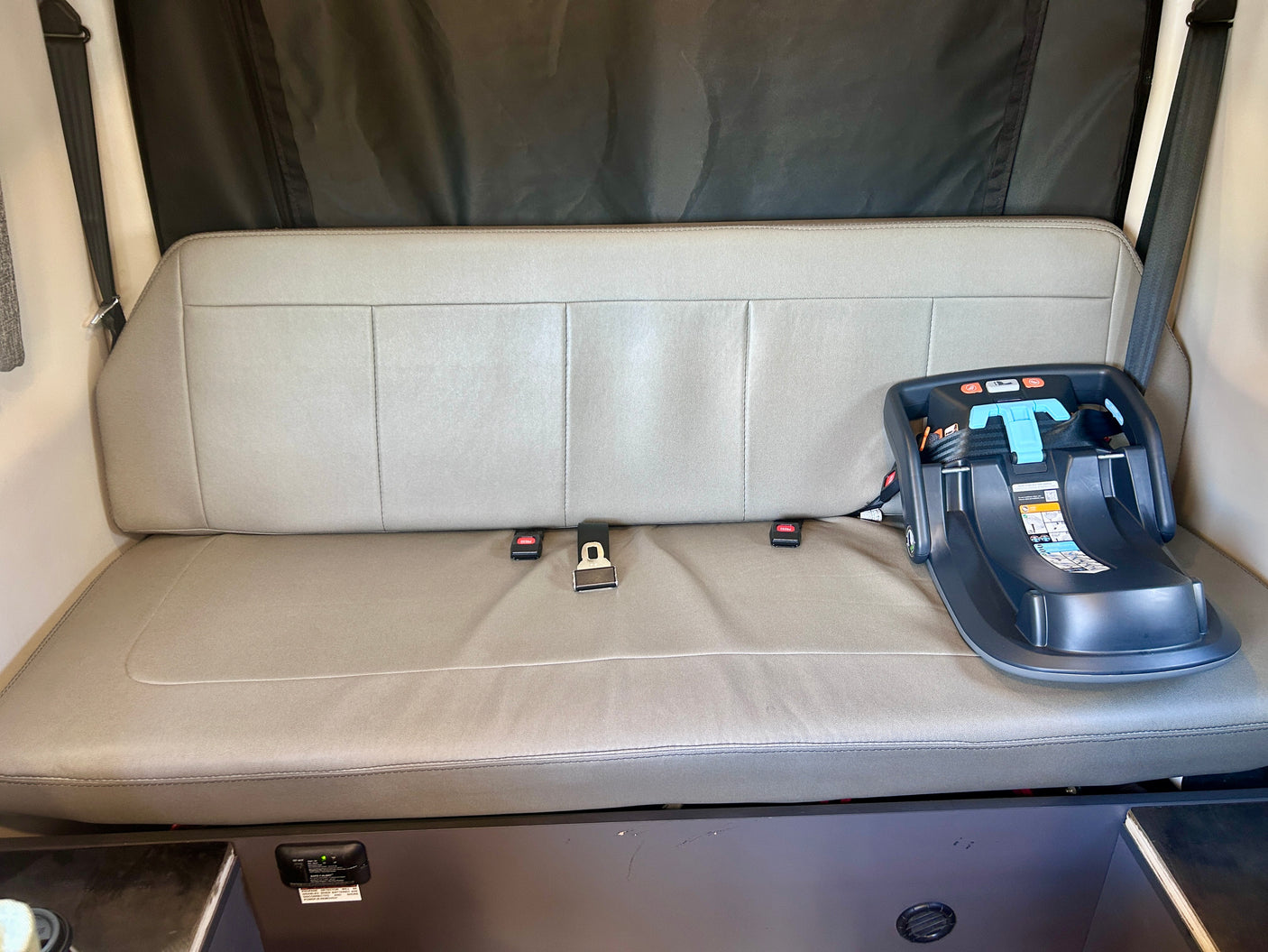 RV rental interior with a gray bench seat, safety belts, and an infant car seat base, ready for family travel.