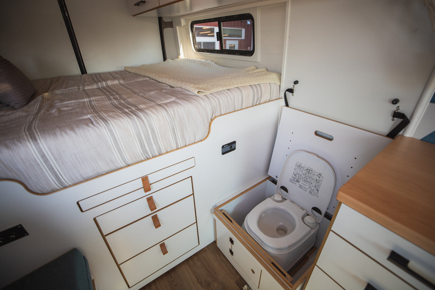 RV rental interior: cozy bed, smart storage drawers, and a discreet pull-out toilet for comfort on the road.