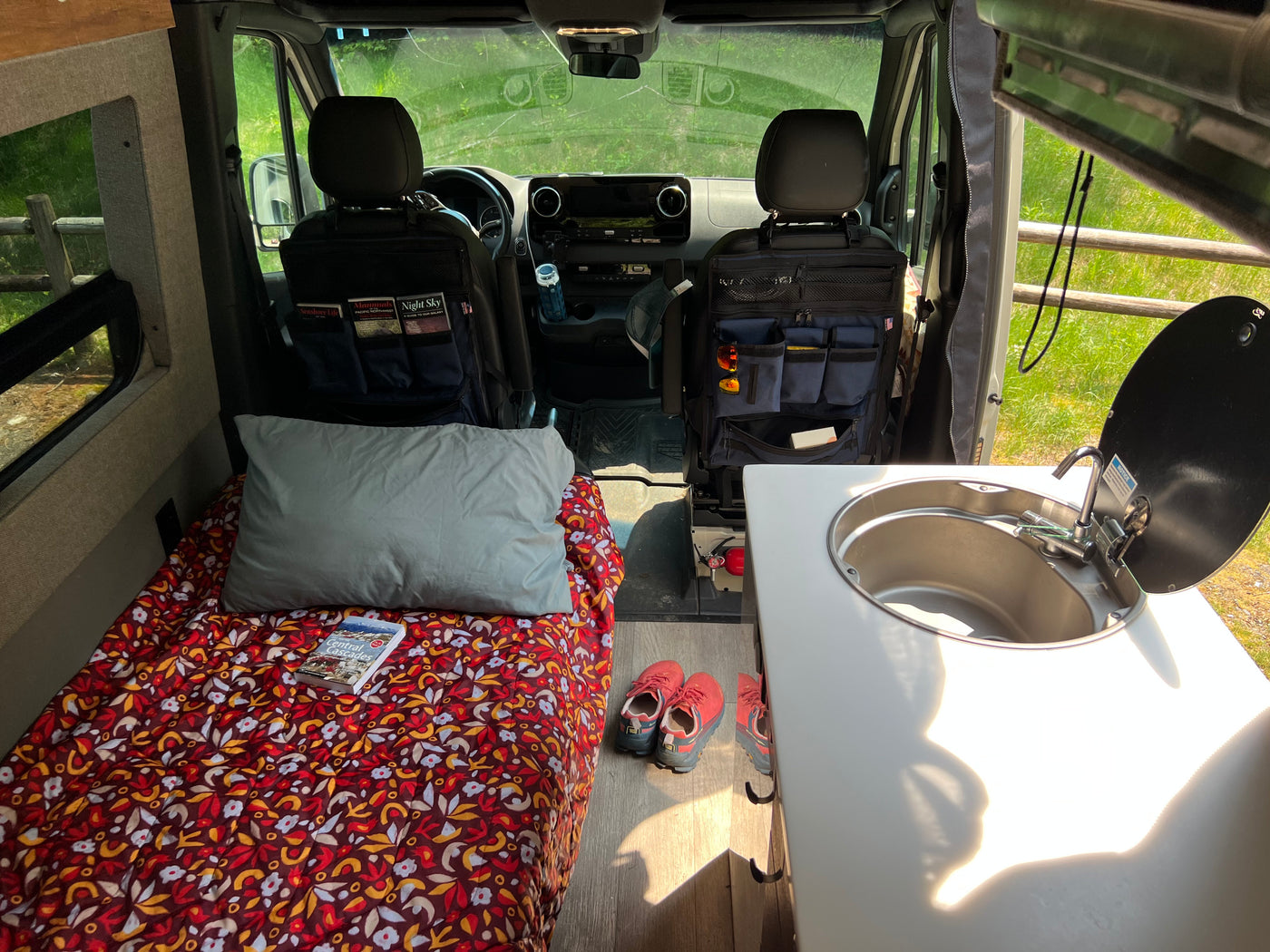 Inside an RV rental: a cozy bed with colorful bedding, a functional kitchen sink, and organized front seats, ready for adventure. — photo 2