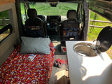 Inside an RV rental: a cozy bed with colorful bedding, a functional kitchen sink, and organized front seats, ready for adventure.