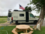 RV rental camper van with US flag, parked by a picnic table, ready for outdoor adventure.