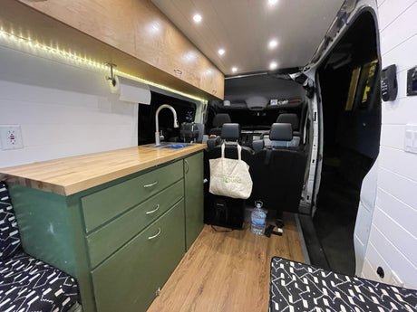 Spacious RV rental interior with custom kitchen, sink, and cabinets. Cozy seating and bright LED lighting create a comfortable mobile living space.