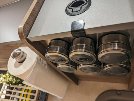 Maximize space in your RV rental! Organized compact kitchen with magnetic spice jars mounted under a cabinet, and a paper towel roll below.
