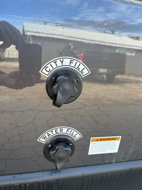 Two water fill ports labeled "CITY FILL" and "WATER FILL" are visible on the side of an RV rental, alongside a safety warning label.