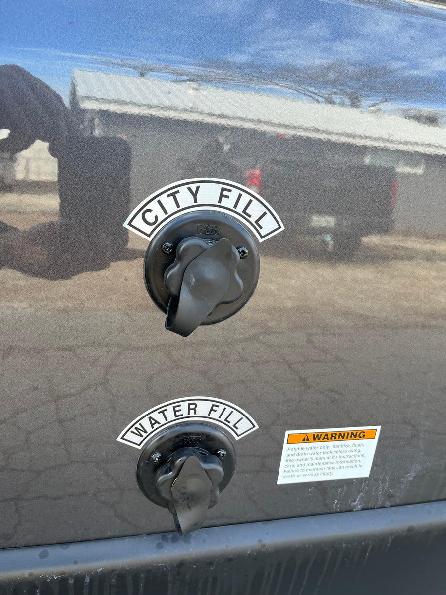 Two water fill ports labeled "CITY FILL" and "WATER FILL" are visible on the side of an RV rental, alongside a safety warning label.