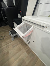 RV rental: Compact van interior with open pull-out trash, black seats, wood floor, and step stool for convenience.