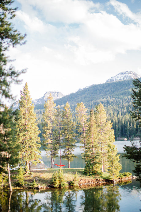 Escape to nature! A red hammock and glamping tent on a lake island, surrounded by forests and mountains. Plan your RV rental getaway.