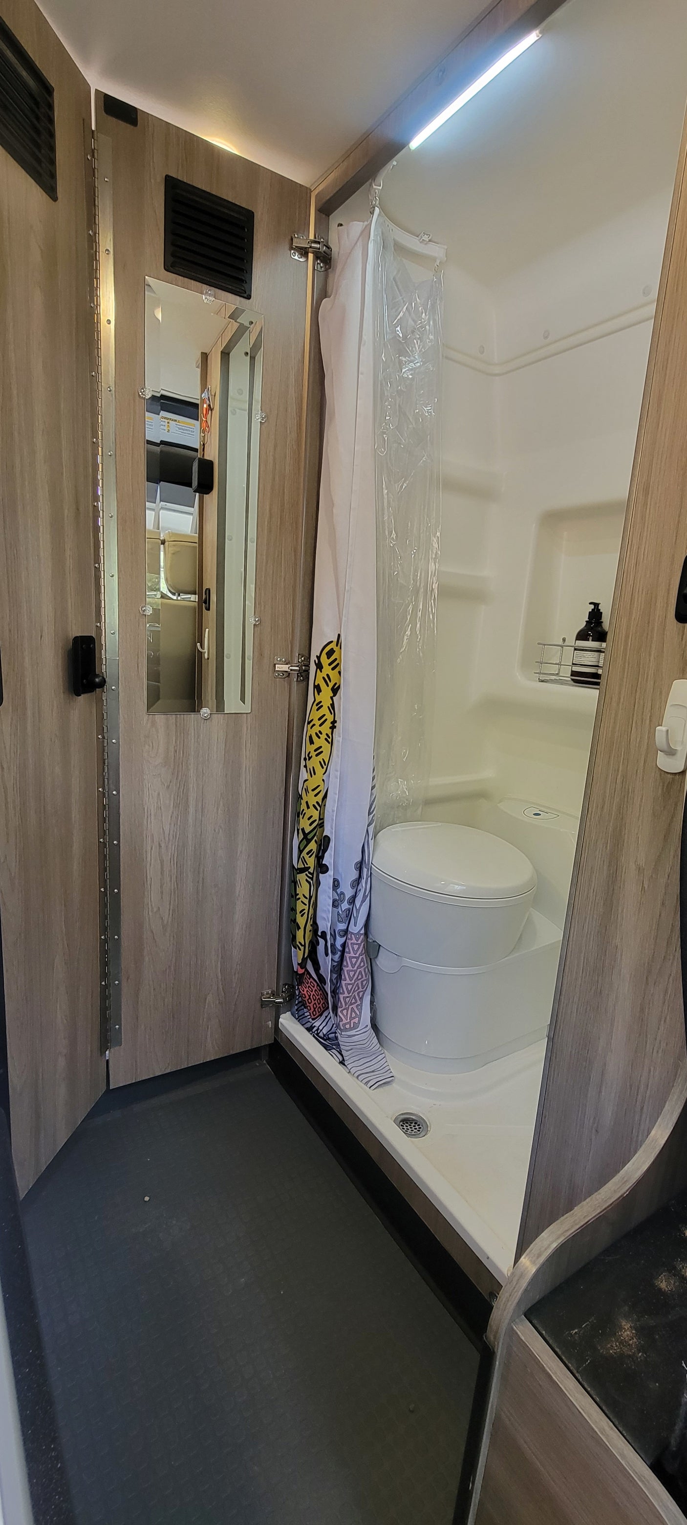 Inside an RV rental, a practical wet bath features a toilet, shower, and mirror, designed for compact living.