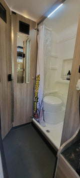 Inside an RV rental, a practical wet bath features a toilet, shower, and mirror, designed for compact living.