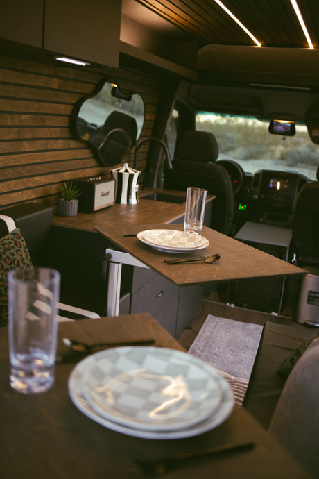 Stylish rv rental interior: wooden walls, compact kitchen with a sink, dining table set with plates, and a Marshall speaker.