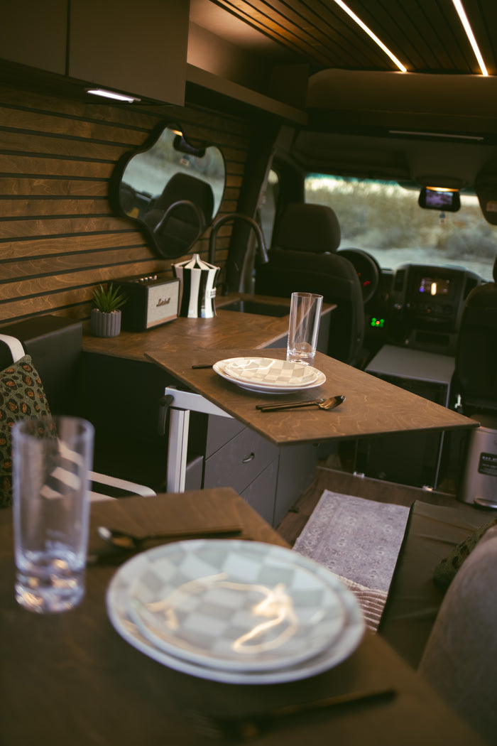 Stylish rv rental interior: wooden walls, compact kitchen with a sink, dining table set with plates, and a Marshall speaker.