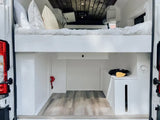 Inside an RV rental: White camper van interior with raised bed, lower cargo/storage area, and wooden ceiling.