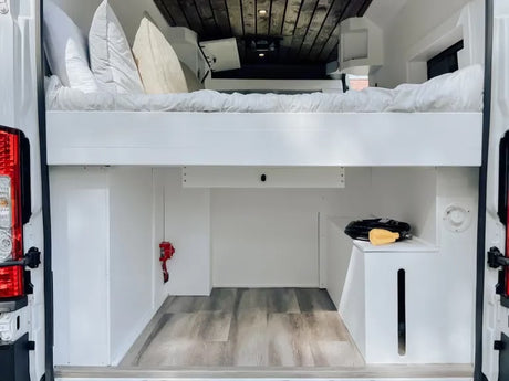 Inside an RV rental: White camper van interior with raised bed, lower cargo/storage area, and wooden ceiling.