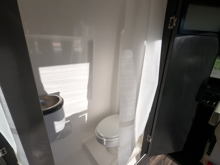 See this bright, compact RV rental bathroom with a toilet, sink, and shower curtain, ideal for travel convenience.