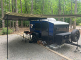 Enjoying the outdoors with this blue Hiker Teardrop Trailer RV rental at a wooded campsite, complete with an extended awning and cooking setup.