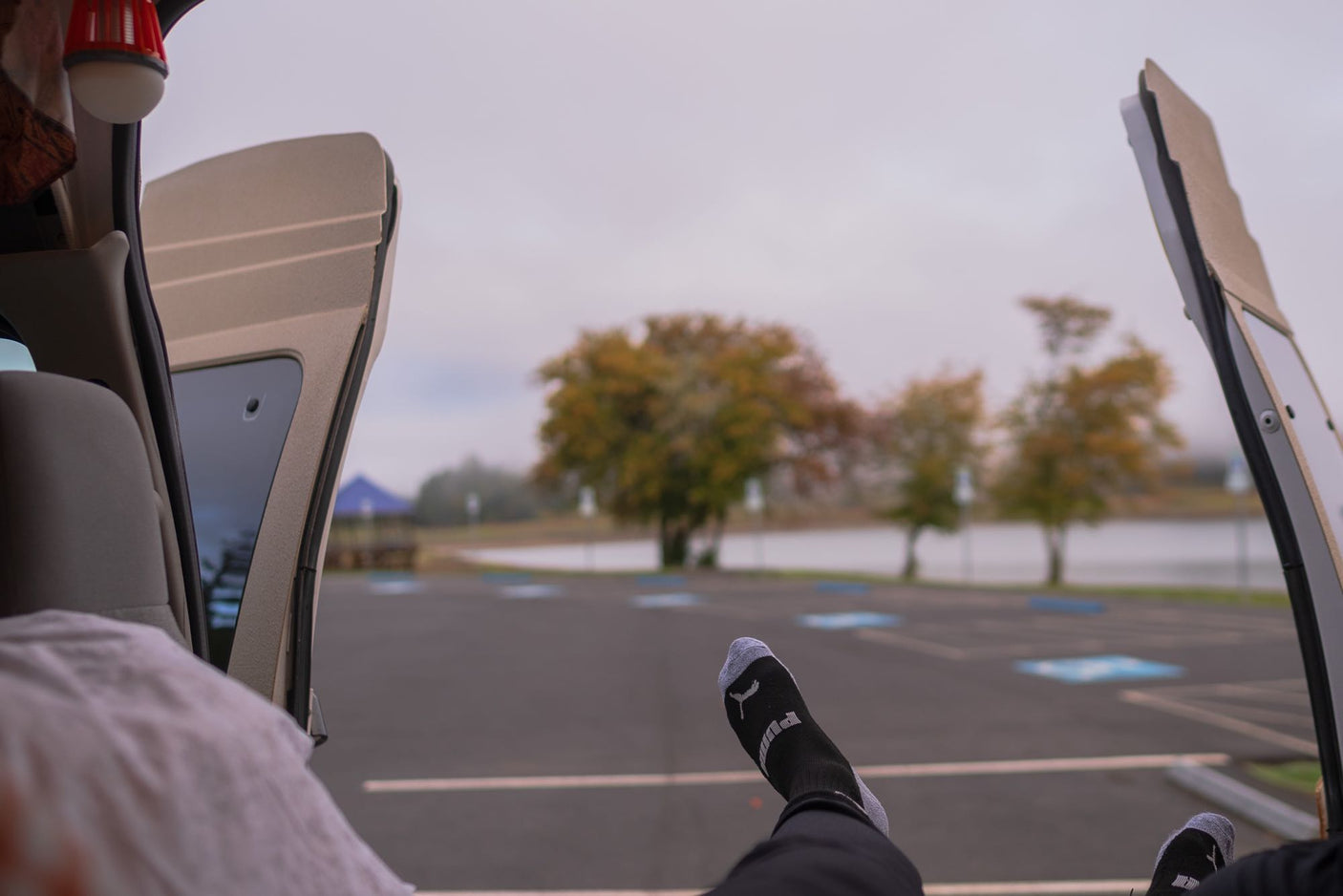 Relaxing inside an RV rental, feet up, enjoying the tranquil lake view and autumn trees from the open back doors.