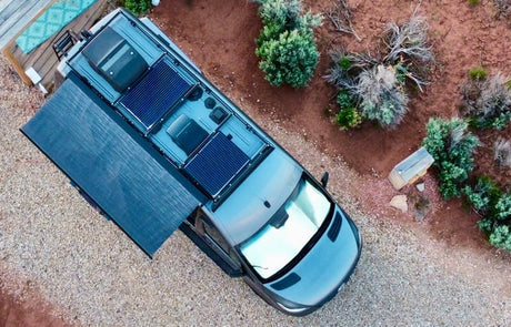 Overhead view of an RV rental with solar panels, awning extended, parked on gravel next to desert landscape. Perfect for adventure!
