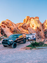 Explore nature's beauty! A Tacoma truck with an RV rental sits amidst majestic red rocks, ready for desert camping.