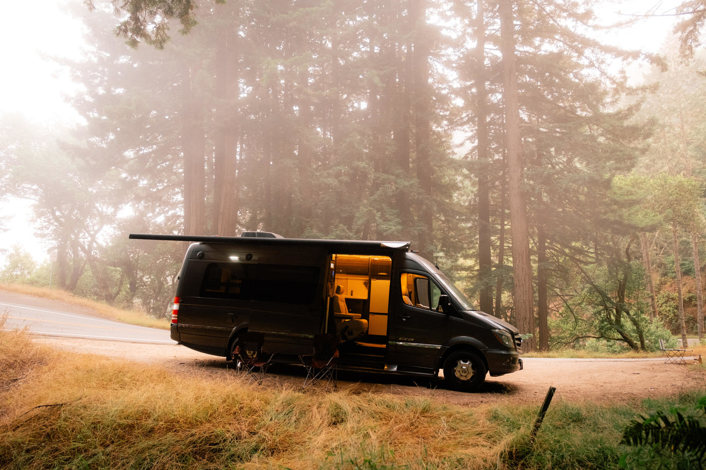 Cozy RV rental adventure. Dark camper van with open door, glowing interior, extended awning, nestled in a misty forest. — photo 3