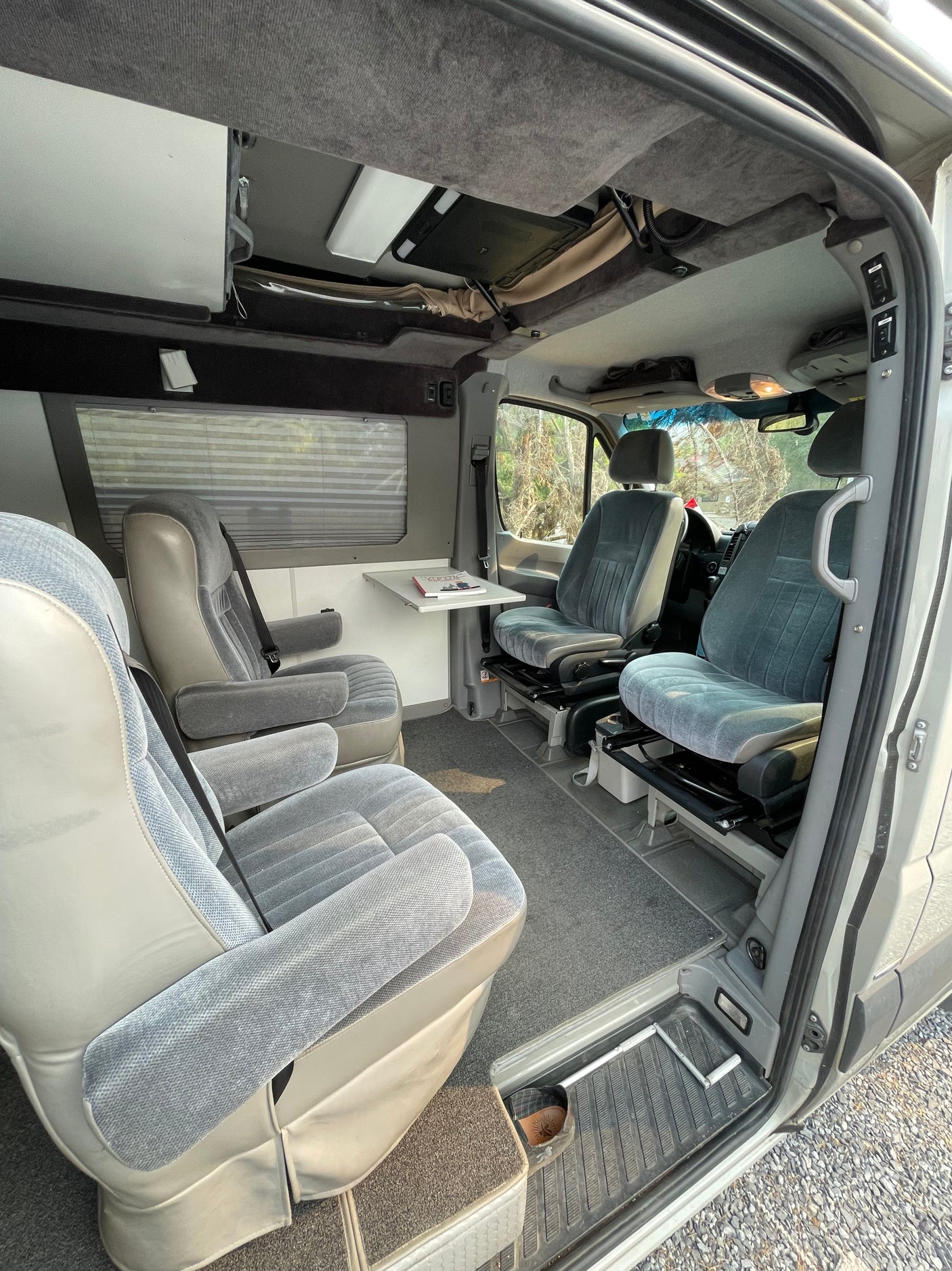Step inside this RV rental! View of grey swivel captain's chairs, comfortable rear seating, and a side table in a clean, carpeted interior.