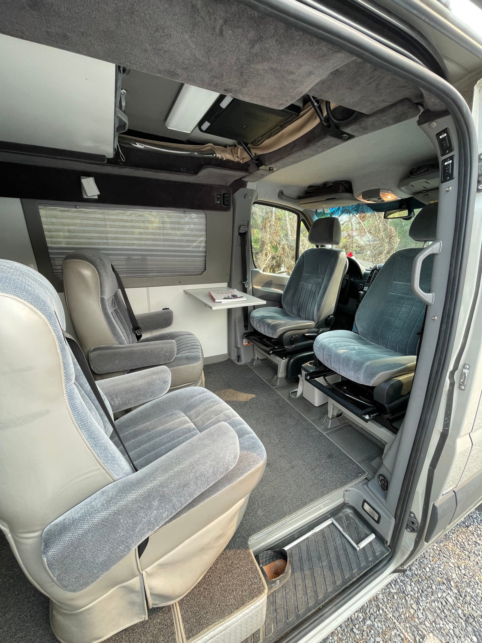 Step inside this RV rental! View of grey swivel captain's chairs, comfortable rear seating, and a side table in a clean, carpeted interior.