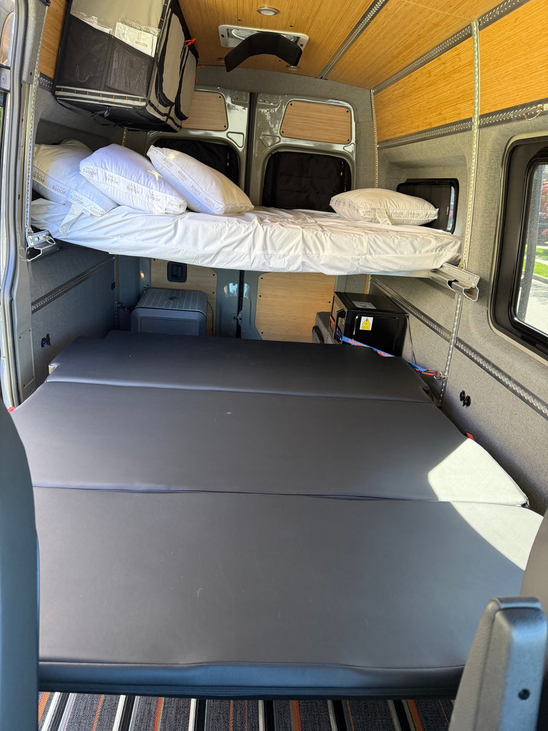 Spacious rv rental interior featuring a raised bed with "Roots Home" pillows and flexible lower cushioned sleeping/seating. — photo 9