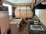 Inside this RV rental: a compact living space featuring a kitchen with stove & sink, a dining area, and sleeping options.