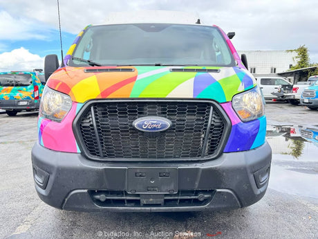 Front of a vibrant, rainbow-wrapped Ford Transit van, likely an rv rental, parked in a wet lot.