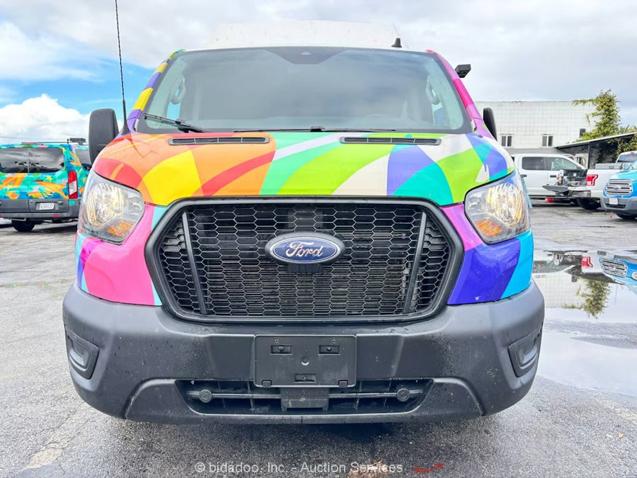 Front of a vibrant, rainbow-wrapped Ford Transit van, likely an rv rental, parked in a wet lot.