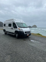 White Winnebago Solis RV rental parked on a gravel lot overlooking the stormy Pacific Ocean and sea stacks.