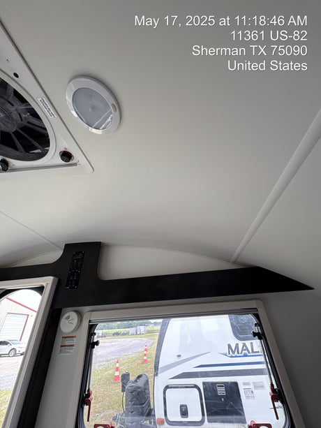 Inside an RV rental, showing overhead fan, light, controls, and an outside view of another RV through the window.