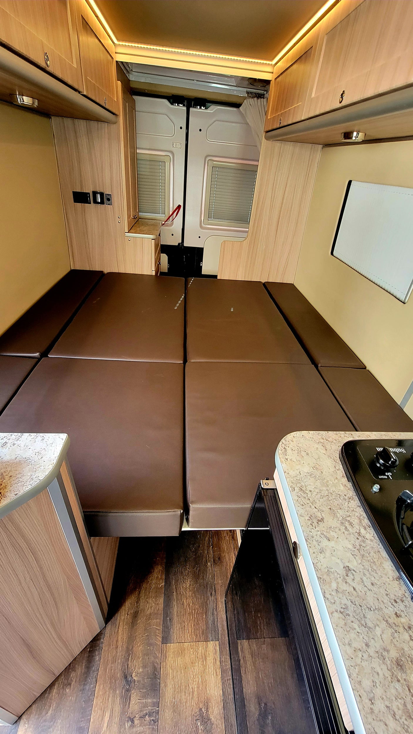 Camper van rv rental: functional interior with a large brown bed, wooden cabinets, and a convenient kitchen.