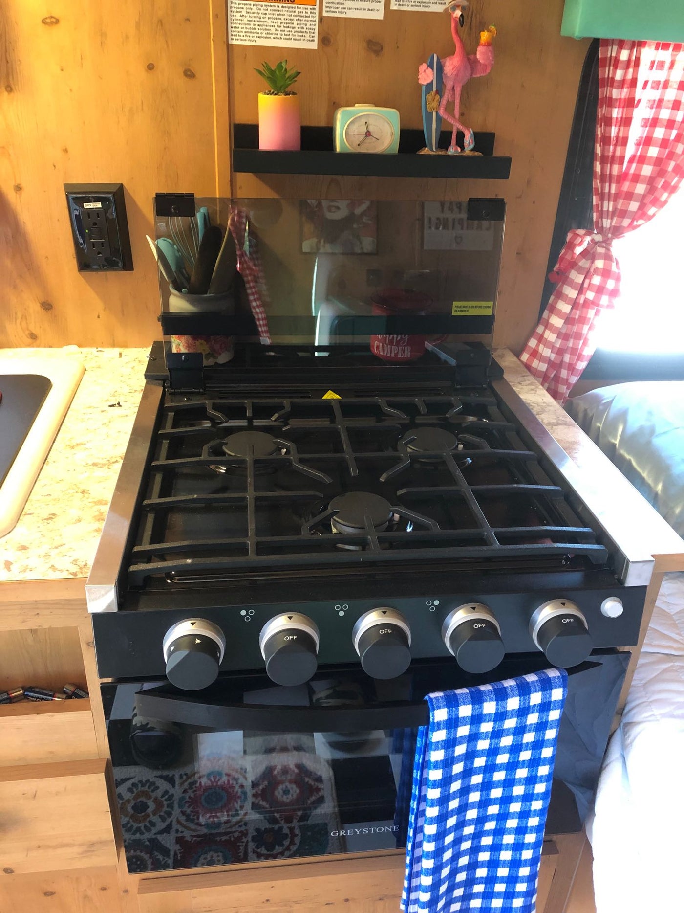 Inside an rv rental, a compact kitchen features a Greystone stove/oven, sink, and colorful decor. — photo 12