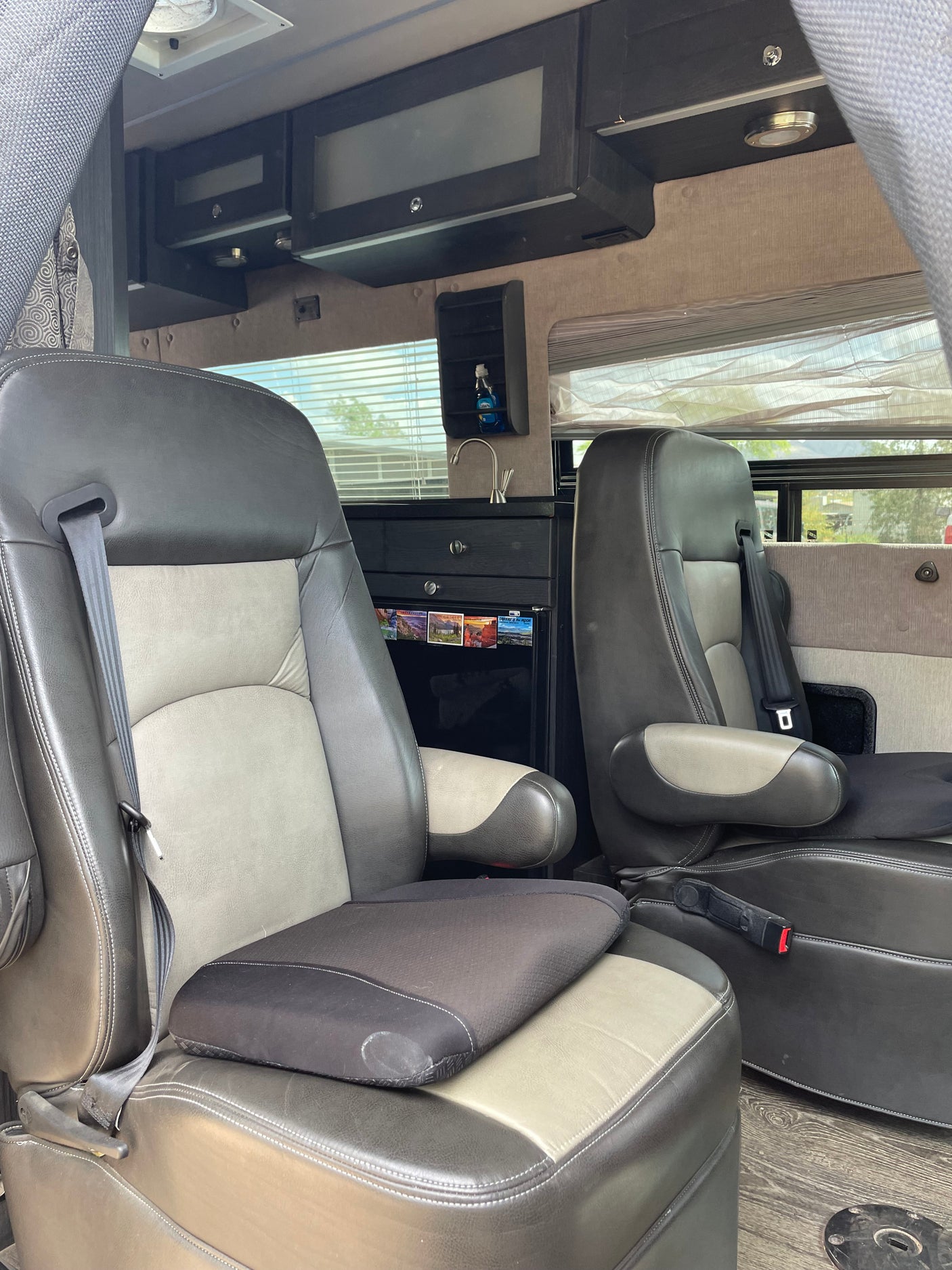 Comfortable two-tone grey/beige passenger seats inside an RV rental. Features include a compact kitchen, sink, and overhead storage.