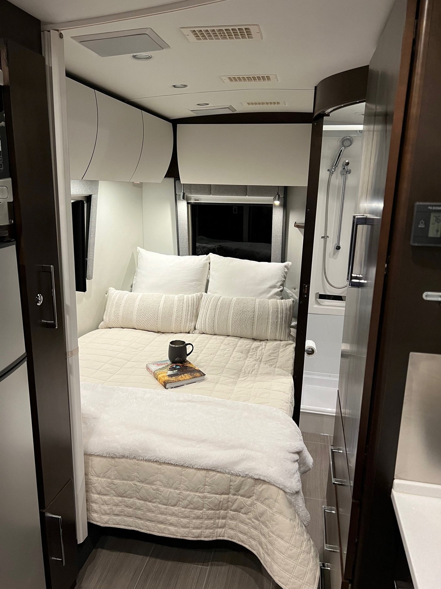 RV rental interior: a cozy bedroom with a modern bed, white cabinets, and compact shower visible on the right.