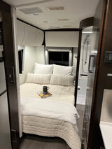 RV rental interior: a cozy bedroom with a modern bed, white cabinets, and compact shower visible on the right.