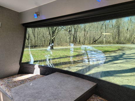 Enjoy the view from your RV rental! Cozy dinette with a large window overlooking a wooded outdoor scene.