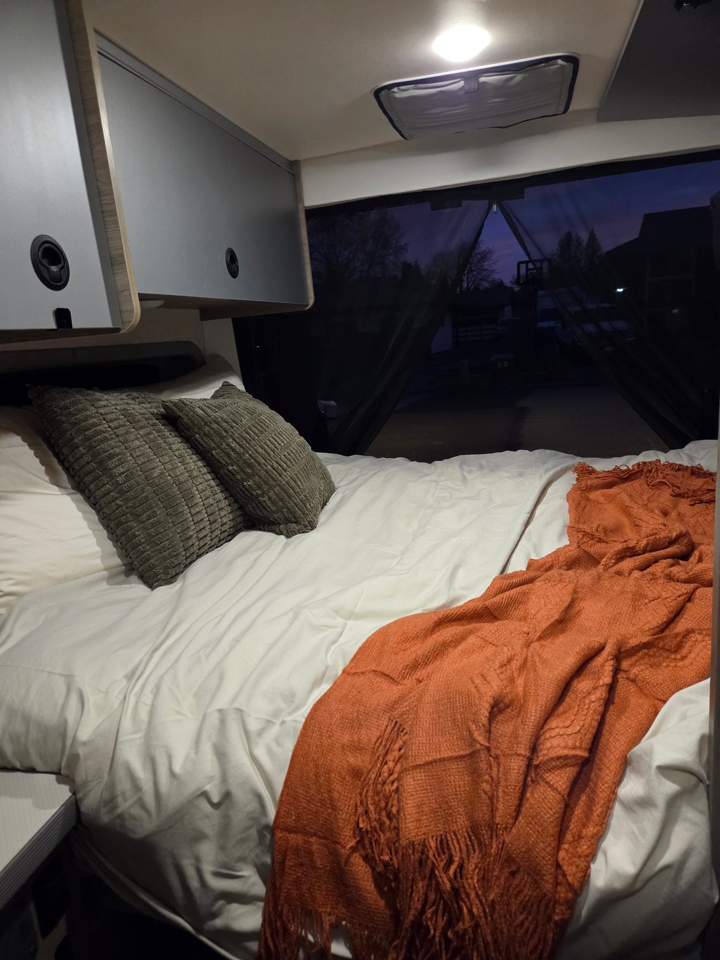 Cozy RV rental bed with textured gray pillows and an orange throw blanket. Perfect for a comfortable night.