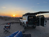 Desert sunset with an overland SUV setup, perfect for an adventurous rv rental getaway, featuring camping gear and awning.