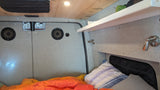 This RV rental features a cozy sleeping area with speakers, wood ceiling, a white shelf, and bedding. Designed for comfort.