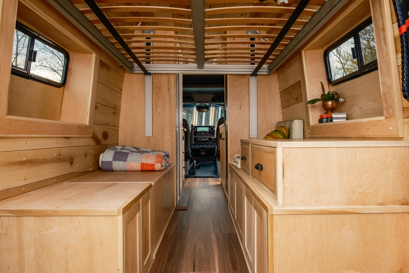 Step inside this cozy rv rental camper van, featuring a beautiful wooden interior with built-in storage, sleeping areas, and a view to the cockpit.