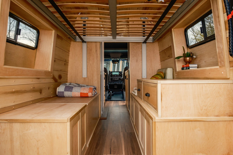 Step inside this cozy rv rental camper van, featuring a beautiful wooden interior with built-in storage, sleeping areas, and a view to the cockpit. — photo 9