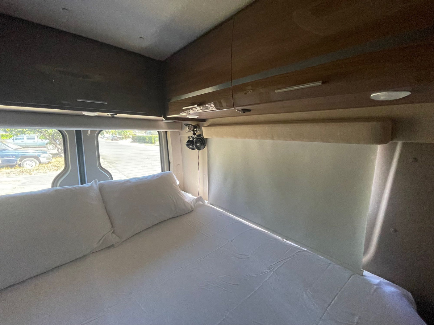 RV rental bedroom with a fresh bed, storage cabinets, and window shades providing privacy and comfort.